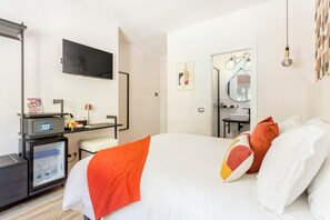 Una camera d'albergo con un letto, una scrivania con un computer, un frigorifero, una televisione e un bagno con uno specchio e un lavandino.