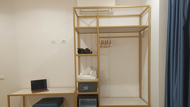 A bedroom with a bed, a desk with a laptop, a wardrobe, and a small storage unit.