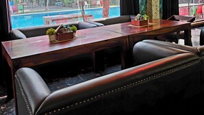 A restaurant with a pool view, outdoor seating, and a wooden table with chairs. - Chopra Farms and Resorts (Gurugram)