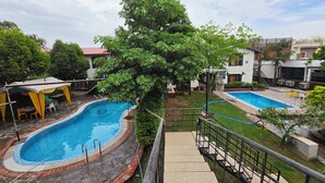 A swimming pool with a stone border, a covered seating area, and a staircase leading to a deck. - Chopra Farms and Resorts (Gurugram)