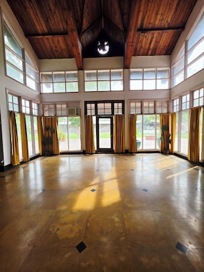 A spacious room with a high ceiling, large windows, and a door leading outside. - Chopra Farms and Resorts (Gurugram)