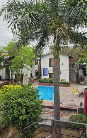 A residential area with a swimming pool, palm trees, and a building with a sign indicating pool rules. - Chopra Farms and Resorts (Gurugram)