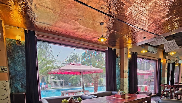 A restaurant with a pool view, leather seating, and patterned ceiling. - Chopra Farms and Resorts (Gurugram)