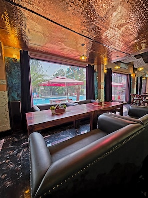 A restaurant with a pool view, leather seating, and patterned ceiling. - Chopra Farms and Resorts (Gurugram)