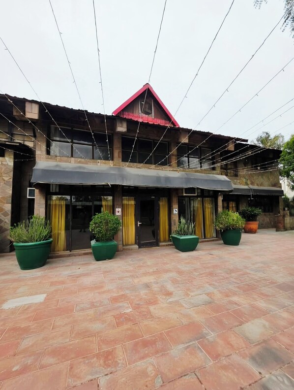 A building with a red roof, large windows, and a covered entrance area with potted plants. - Chopra Farms and Resorts (Gurugram)