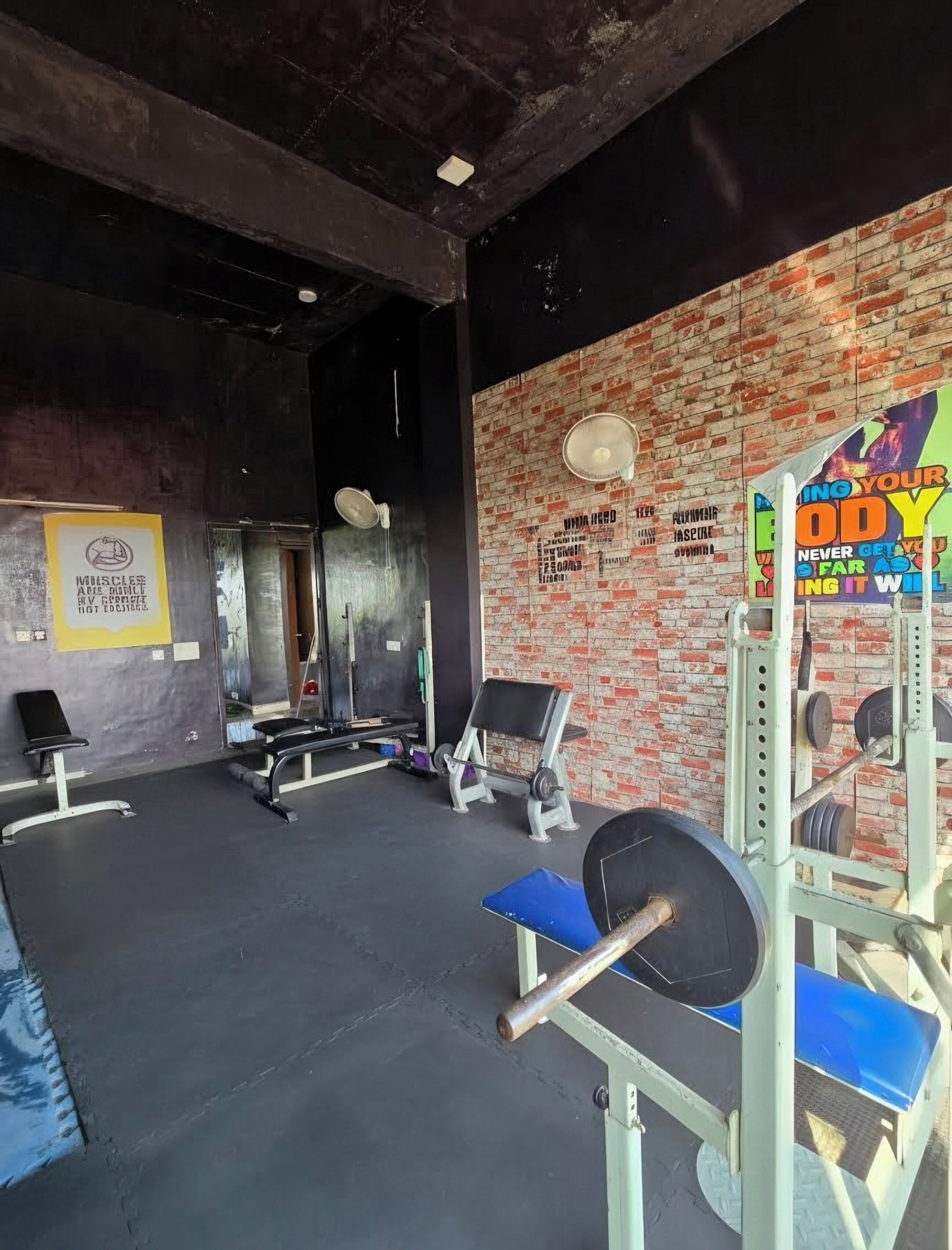 A gym with brick walls, weightlifting equipment, benches, and a mirror.