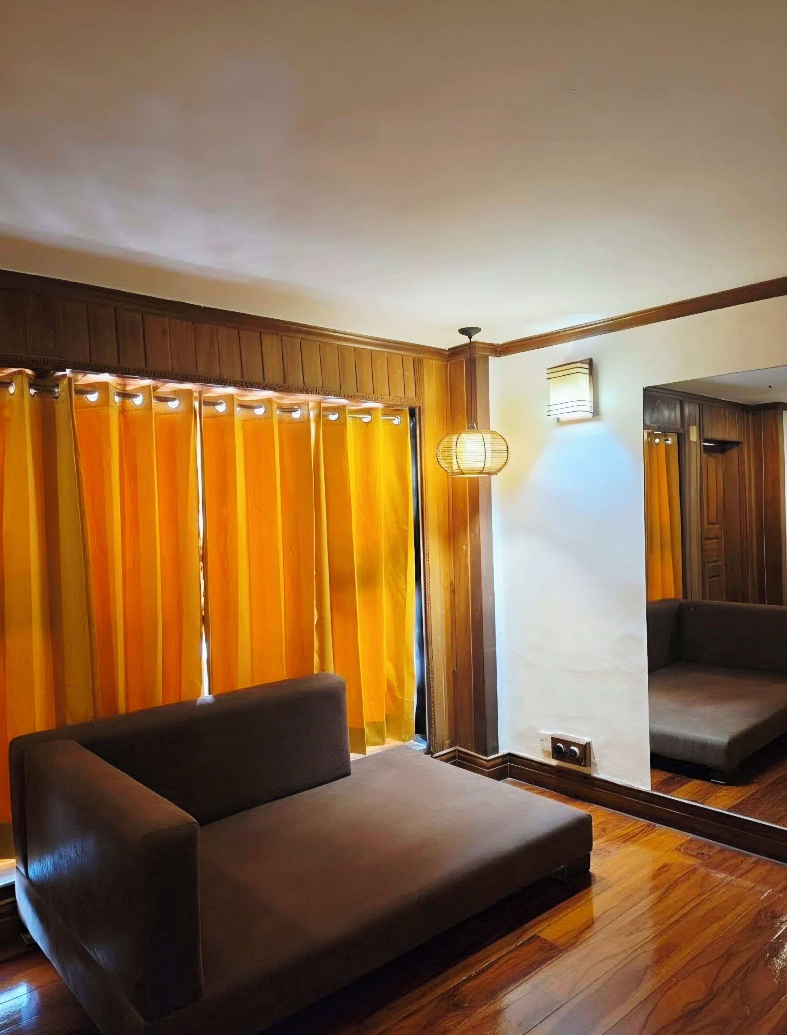Una habitación con sofá, suelo de madera, espejo y cortinas.