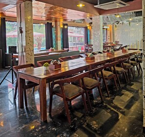 A long wooden table with chairs, a tiled floor, and a view of greenery outside. - Chopra Farms and Resorts (Gurugram)