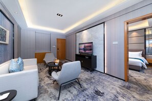 A modern hotel room with a sofa, armchair, dining table, TV, and a bed. - deluxe king (Shenzhen)