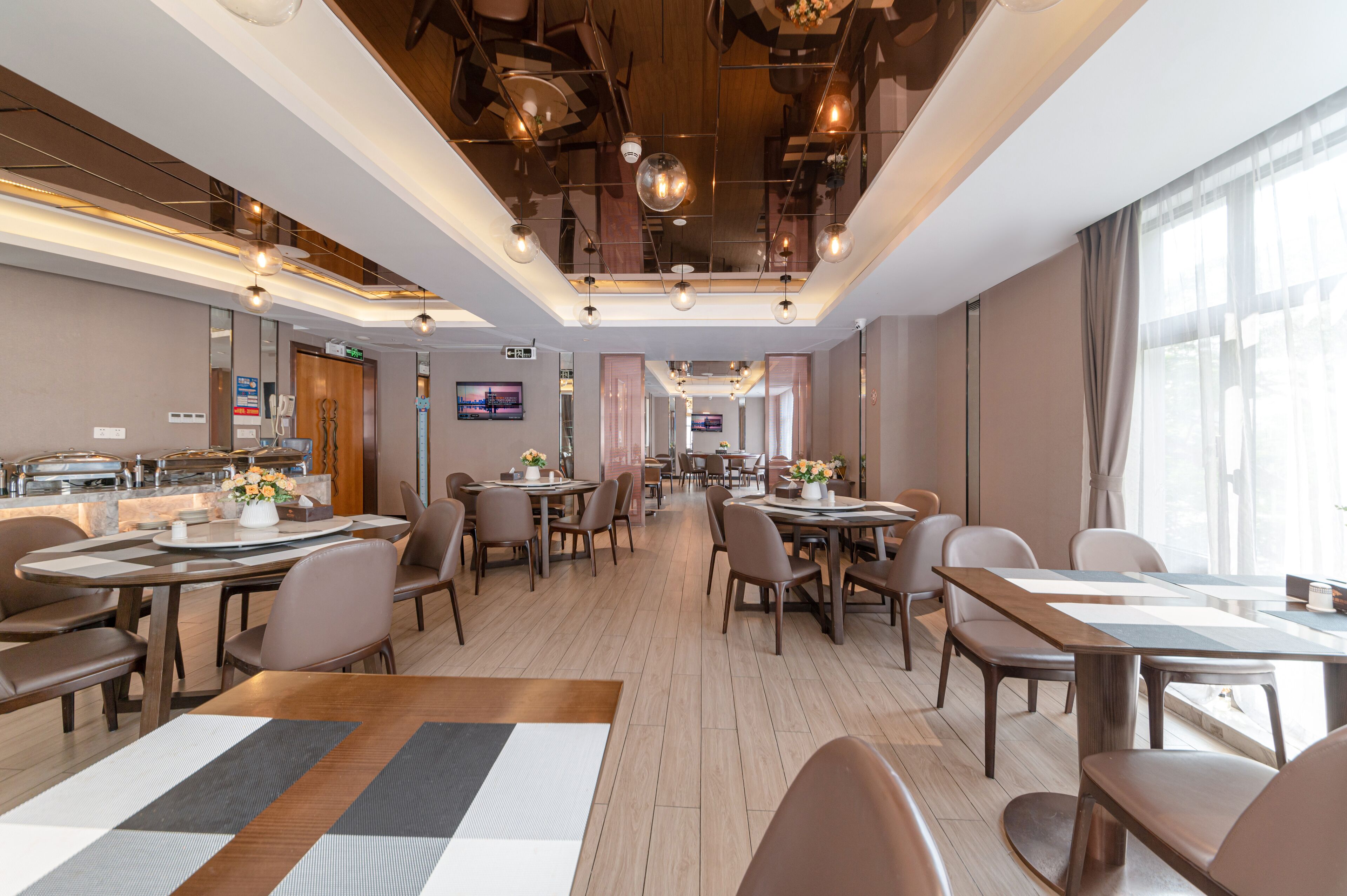 A modern dining area with multiple tables and chairs, a wooden ceiling, and a television screen on the wall.