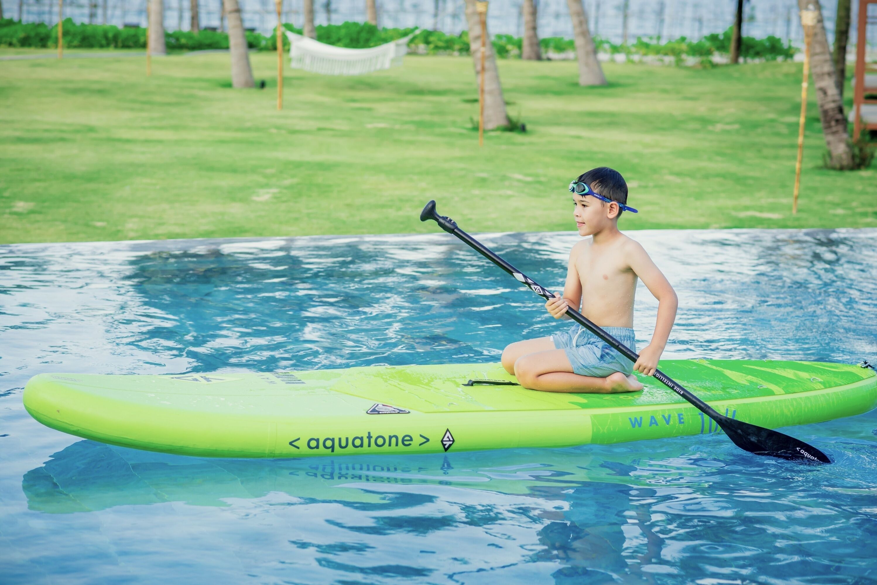 A person sitting on a green paddleboard in a swimming pool.