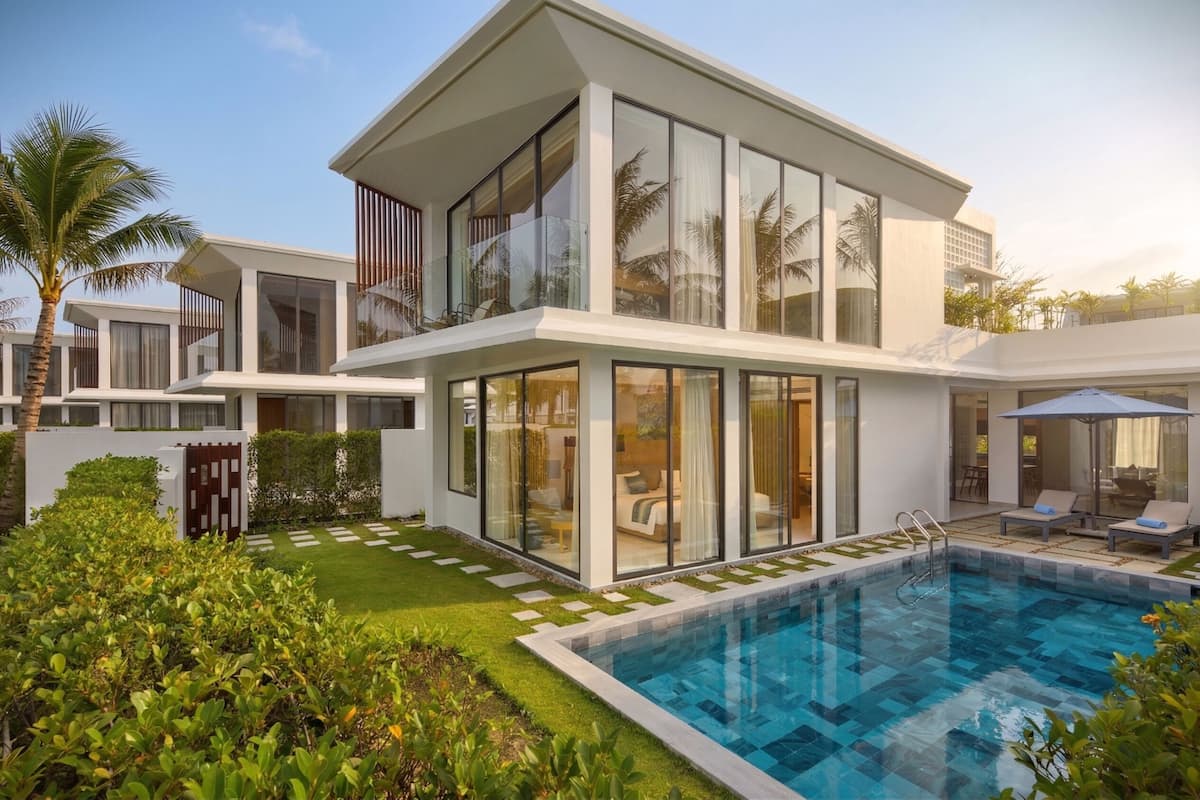 Una casa moderna de dos pisos con piscina, puertas de vidrio y un jardín bien cuidado.
