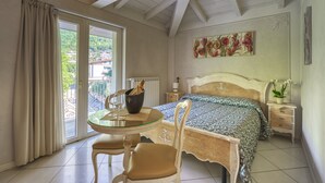 A bedroom with a bed, a bedside table, a chair, a glass table with a bowl and wine glass, and a window with curtains.