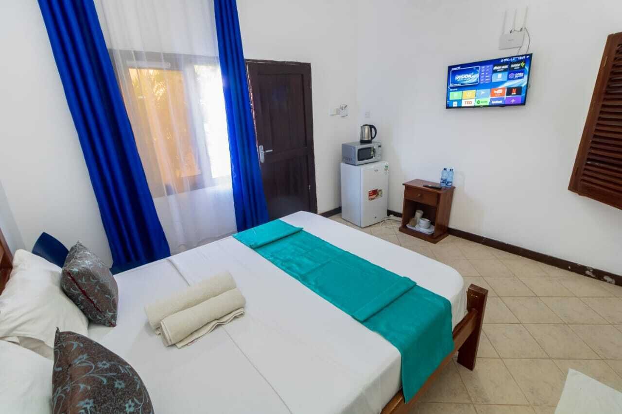 Een hotelkamer met een bed, een aan de muur bevestigde televisie, een klein tafeltje met een waterkoker en een deur.
