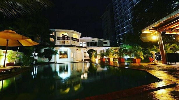 A nighttime view of a hotel with a swimming pool, reflecting the building and palm trees. - Pontoon Residence & Suites (Mombasa)