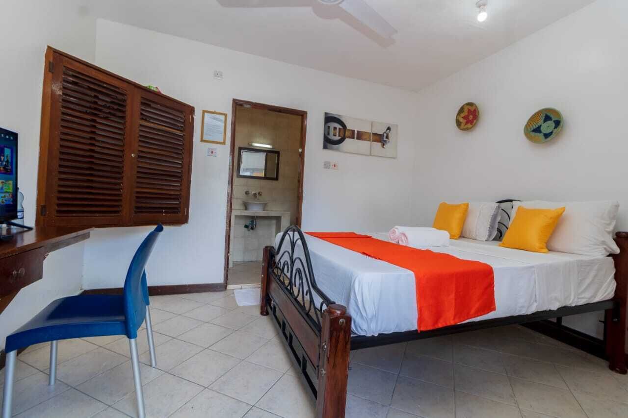 Un dormitorio con cama, escritorio, silla y baño visible a través de una puerta abierta.