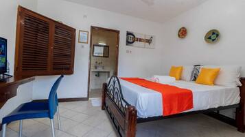 Un dormitorio con cama, escritorio, silla y baño visible a través de una puerta abierta.