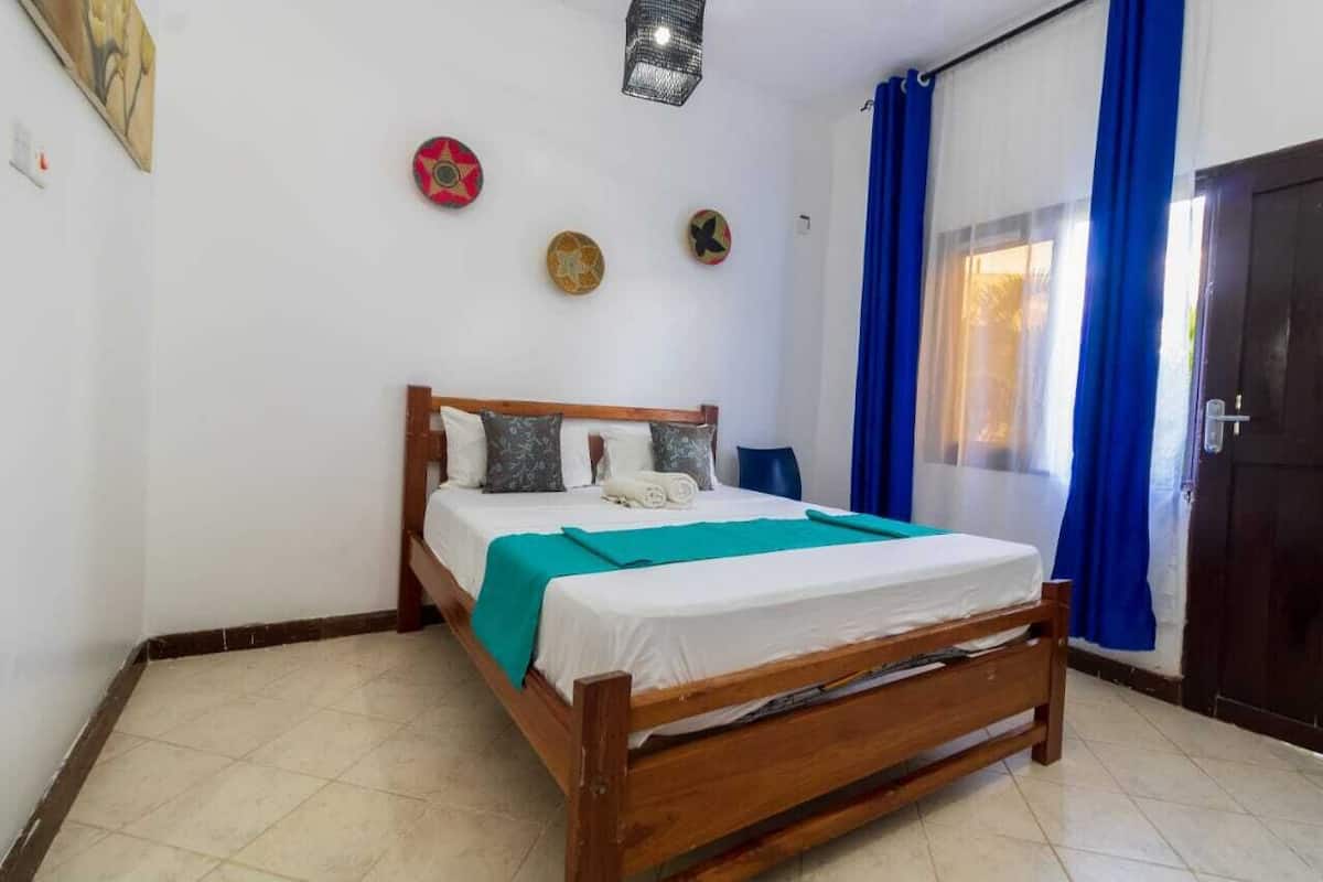A bedroom with a wooden bed, white bedding, a teal throw, and decorative wall hangings.