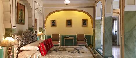 Un dormitorio lujoso con una cama ornamentada, un ventilador de techo y obras de arte enmarcadas en las paredes.