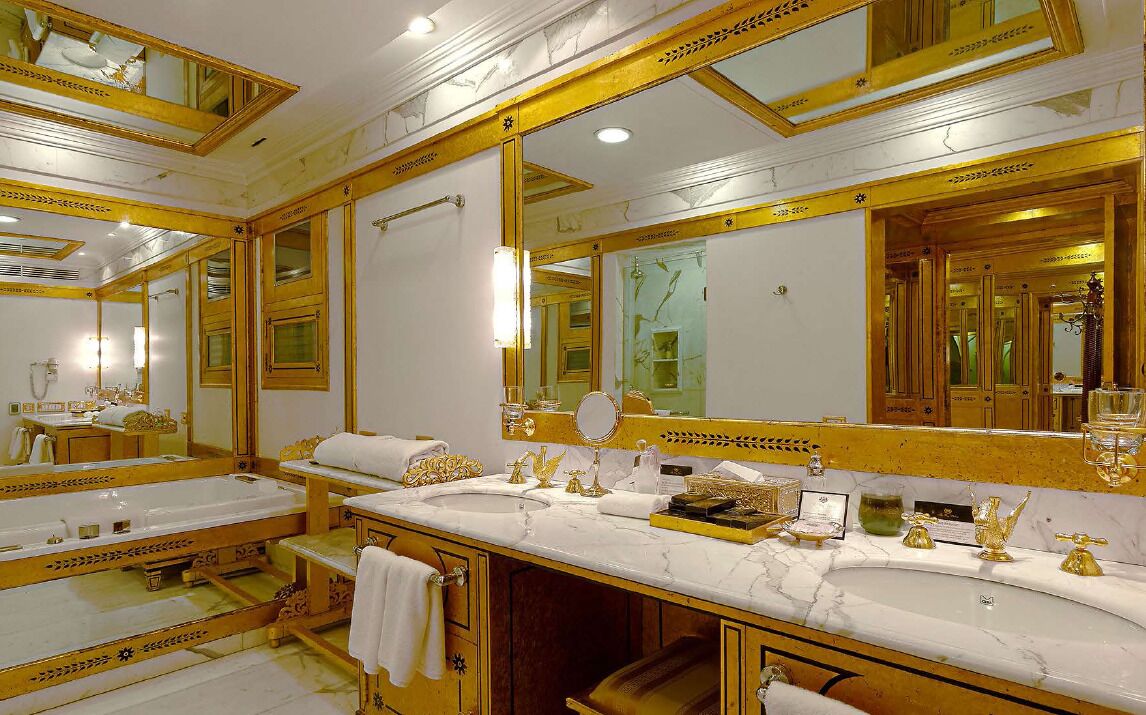 Une salle de bain luxueuse avec des miroirs à cadre doré, des comptoirs en marbre et des accessoires dorés.
