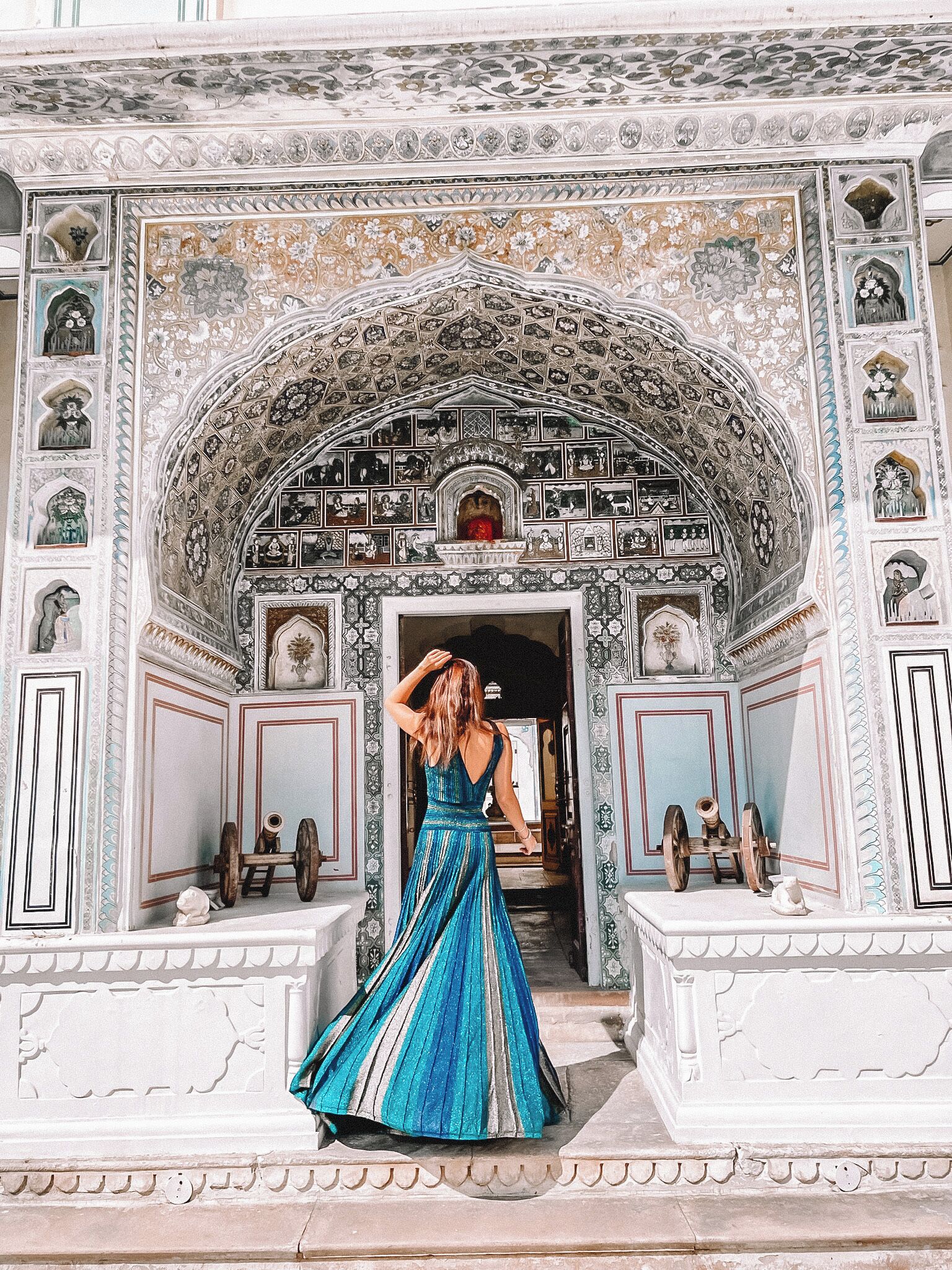 A woman in a blue dress standing in front of a building with intricate tile work and a large archway.