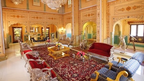 Una sala amplia con candelabros ornamentados, un sofá rojo grande y una alfombra estampada.