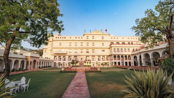 A large, multi-story building with a central courtyard, surrounded by trees and featuring a prominent entrance with a flag.
