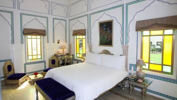 A traditional room with a large bed, two chairs, a small table with a lamp, and a decorative wall painting.