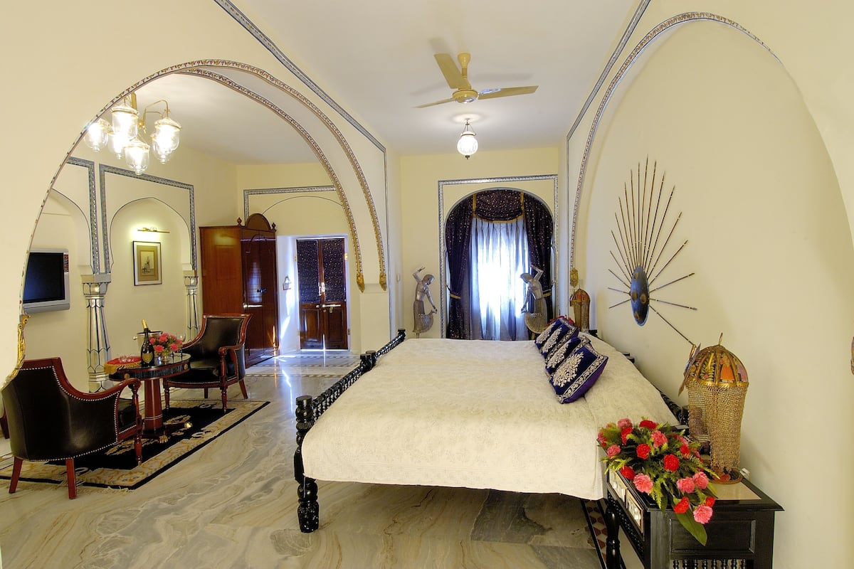 A spacious bedroom with a large bed, two chairs, a small table, and a decorative lamp.