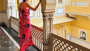 A woman standing on a balcony with ornate railings and a view of a yellow building with traditional architecture. - The Raj Palace (Jaipur)