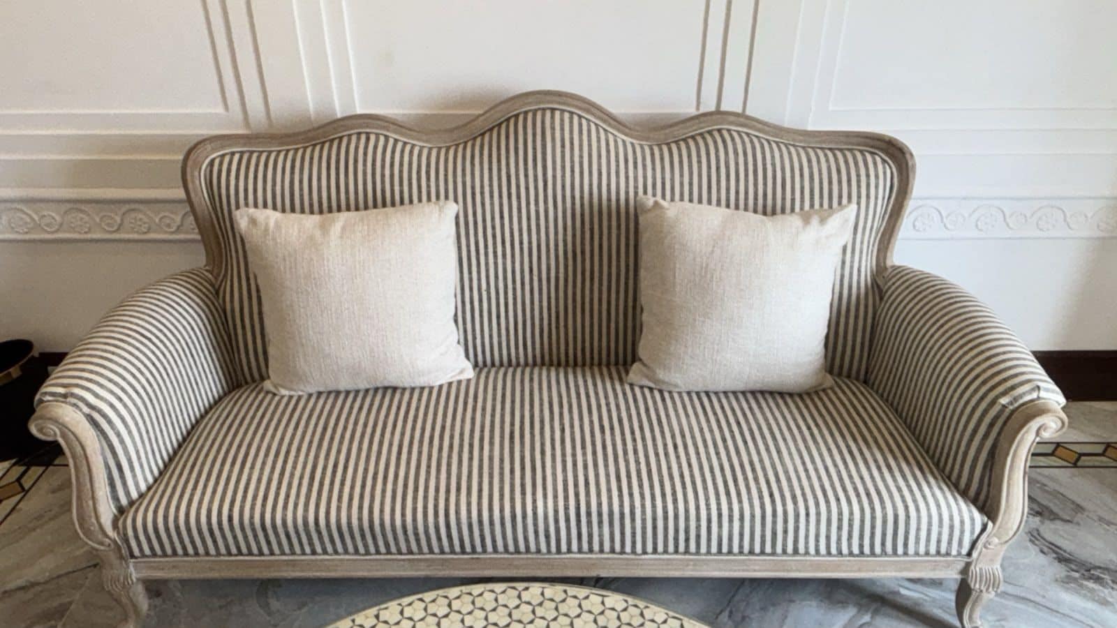 A striped sofa with two cushions against a wall with decorative molding.