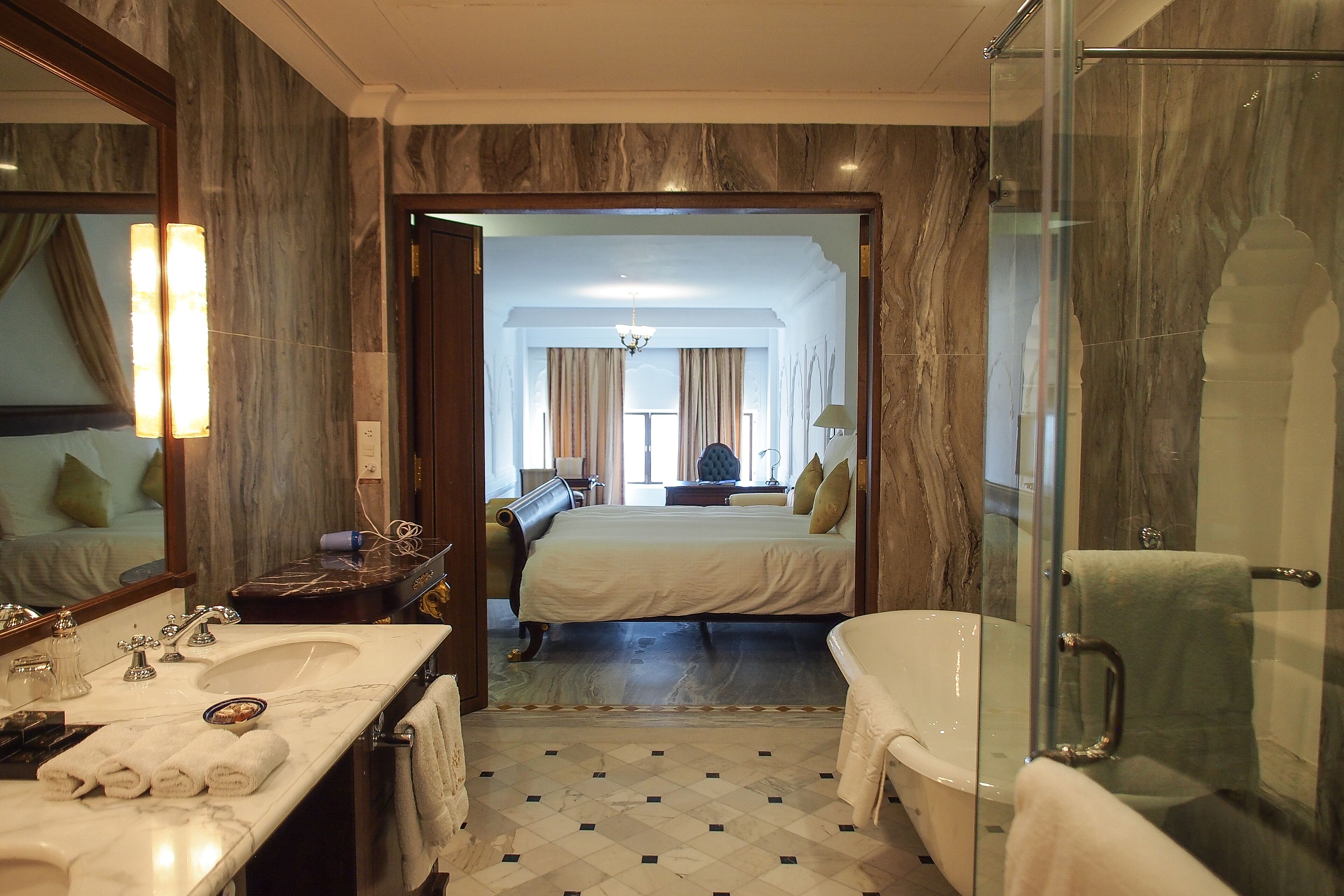 A hotel bathroom with a marble floor, a large mirror, a sink, and a bathtub.