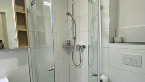 Une cabine de douche fermée par des parois en verre, dotée d’un pommeau de douche à main et d’un robinet mural.