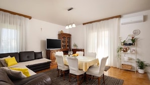 A living room with a sofa, dining table, chairs, a TV, and a cabinet. - Coastal Comfort Apartment (Podstrana)