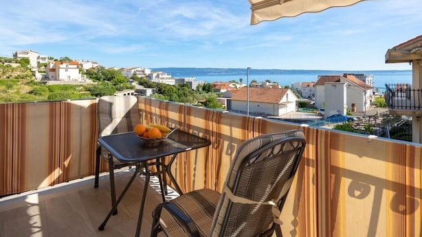 A balcony with a table and chairs, overlooking a coastal town and sea. - Coastal Comfort Apartment (Podstrana)