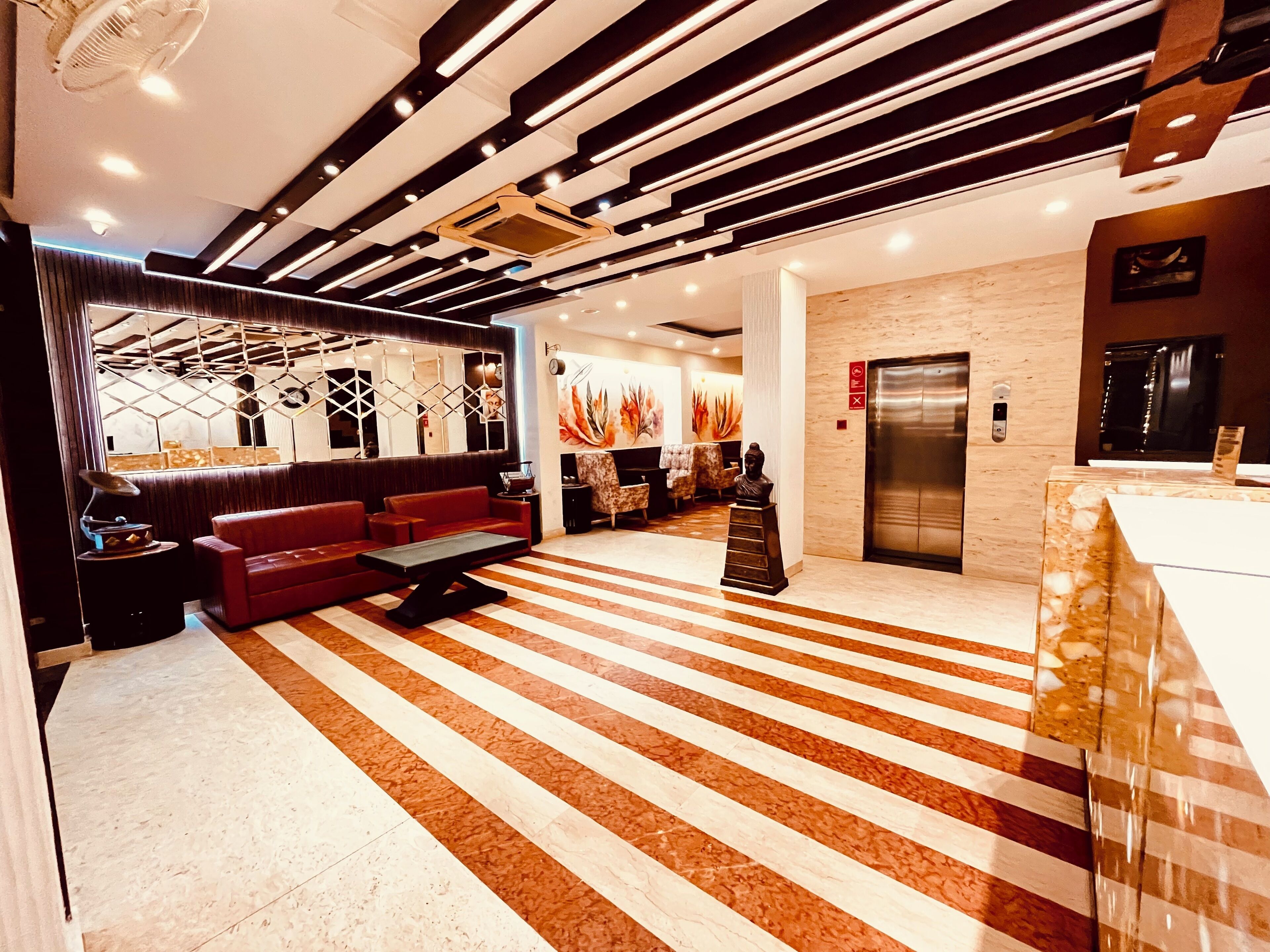 A modern lobby with a striped floor, a seating area with a sofa and a table, a statue, and an elevator.