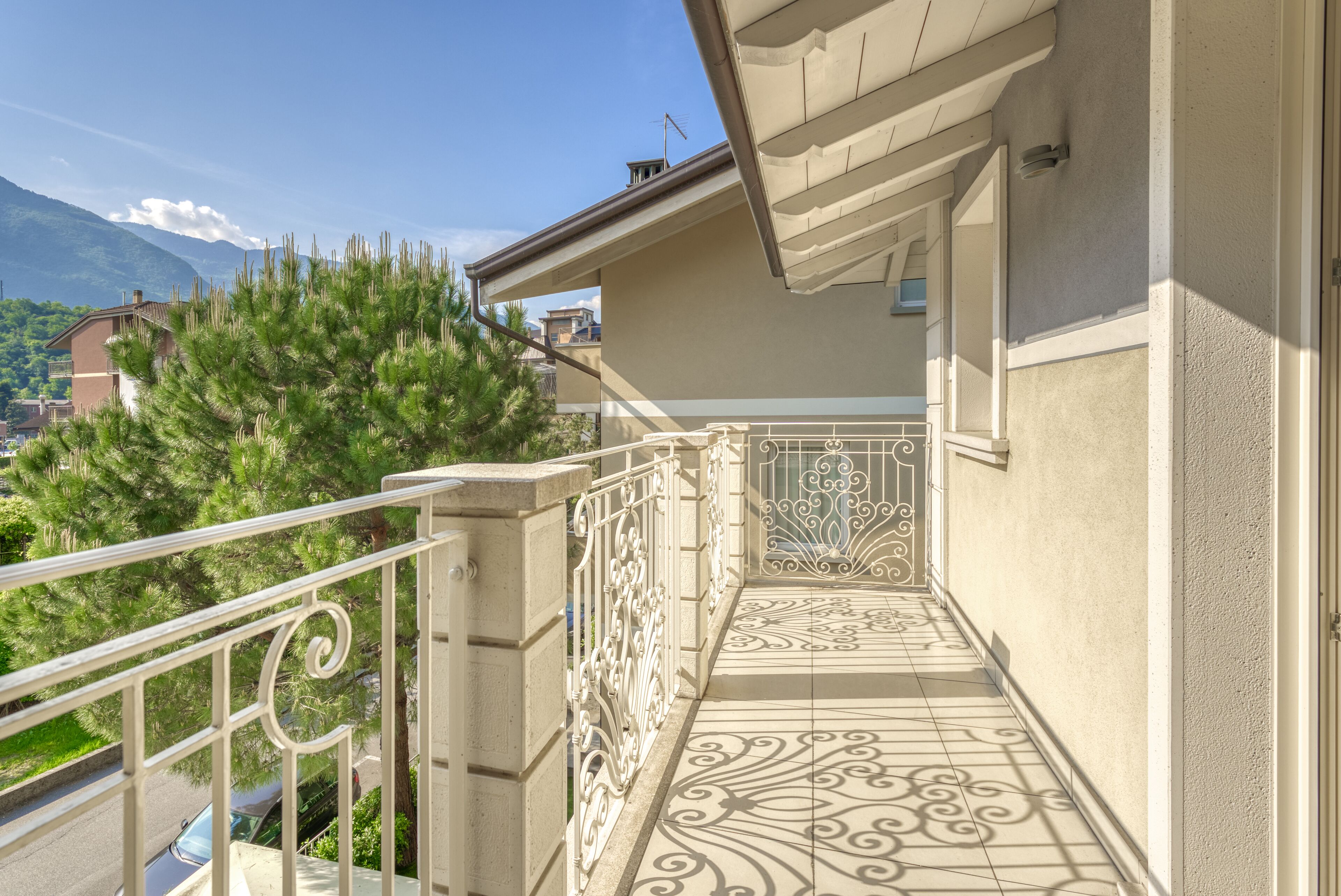 Een balkon met gedetailleerde metalen balustrades en patroonmozaïek vloertegels, met uitzicht op een woonwijk met huizen en een berg op de achtergrond.