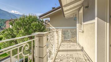 Een balkon met gedetailleerde metalen balustrades en patroonmozaïek vloertegels, met uitzicht op een woonwijk met huizen en een berg op de achtergrond.