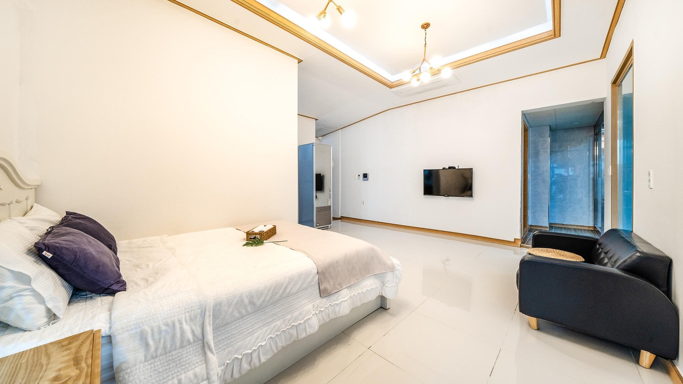 A modern bedroom with a bed, a TV, a sofa, and a large mirror.