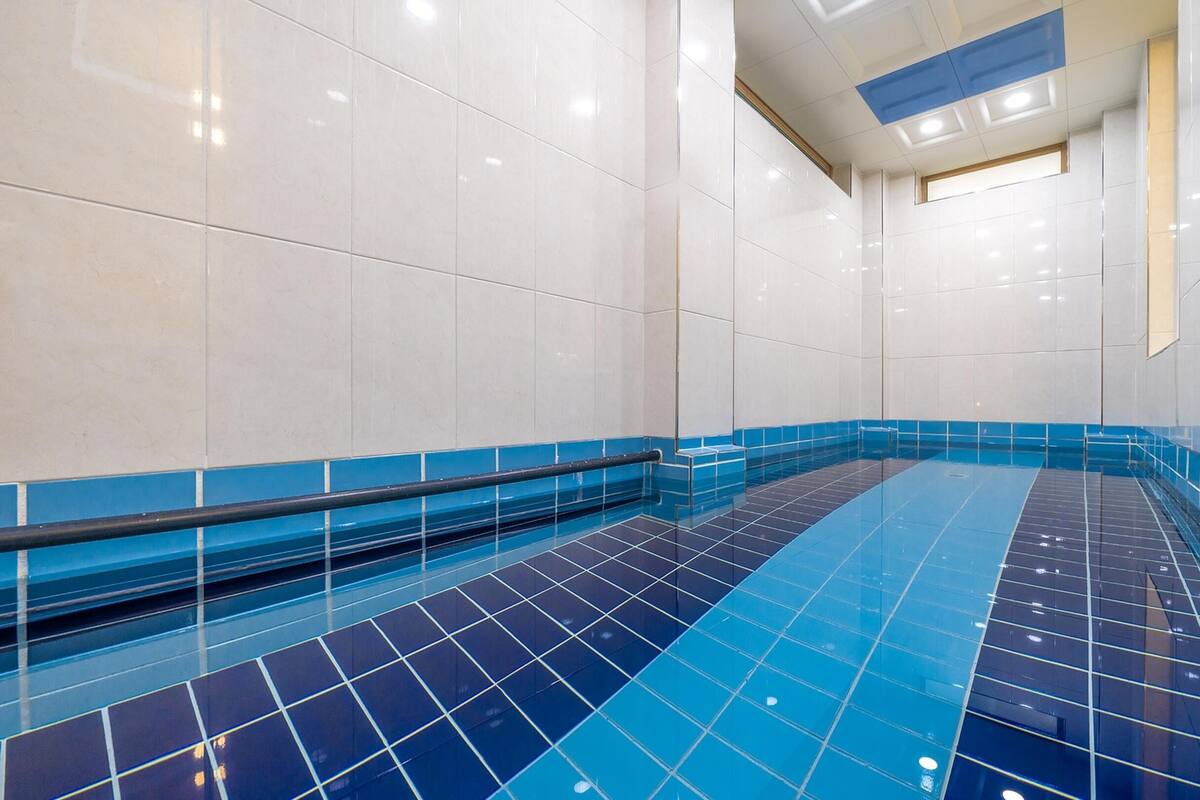 Una piscina con suelos y paredes de baldosas azules y blancas, rodeada de paredes de baldosas blancas y un borde de baldosas azules.