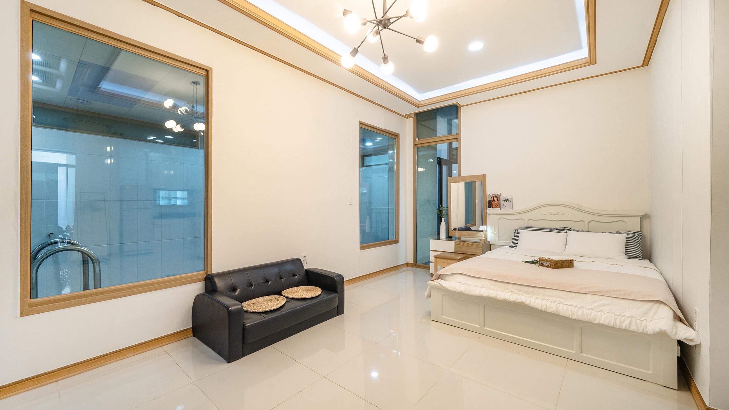 A modern bedroom with a large bed, a black leather sofa, and a glass wall.