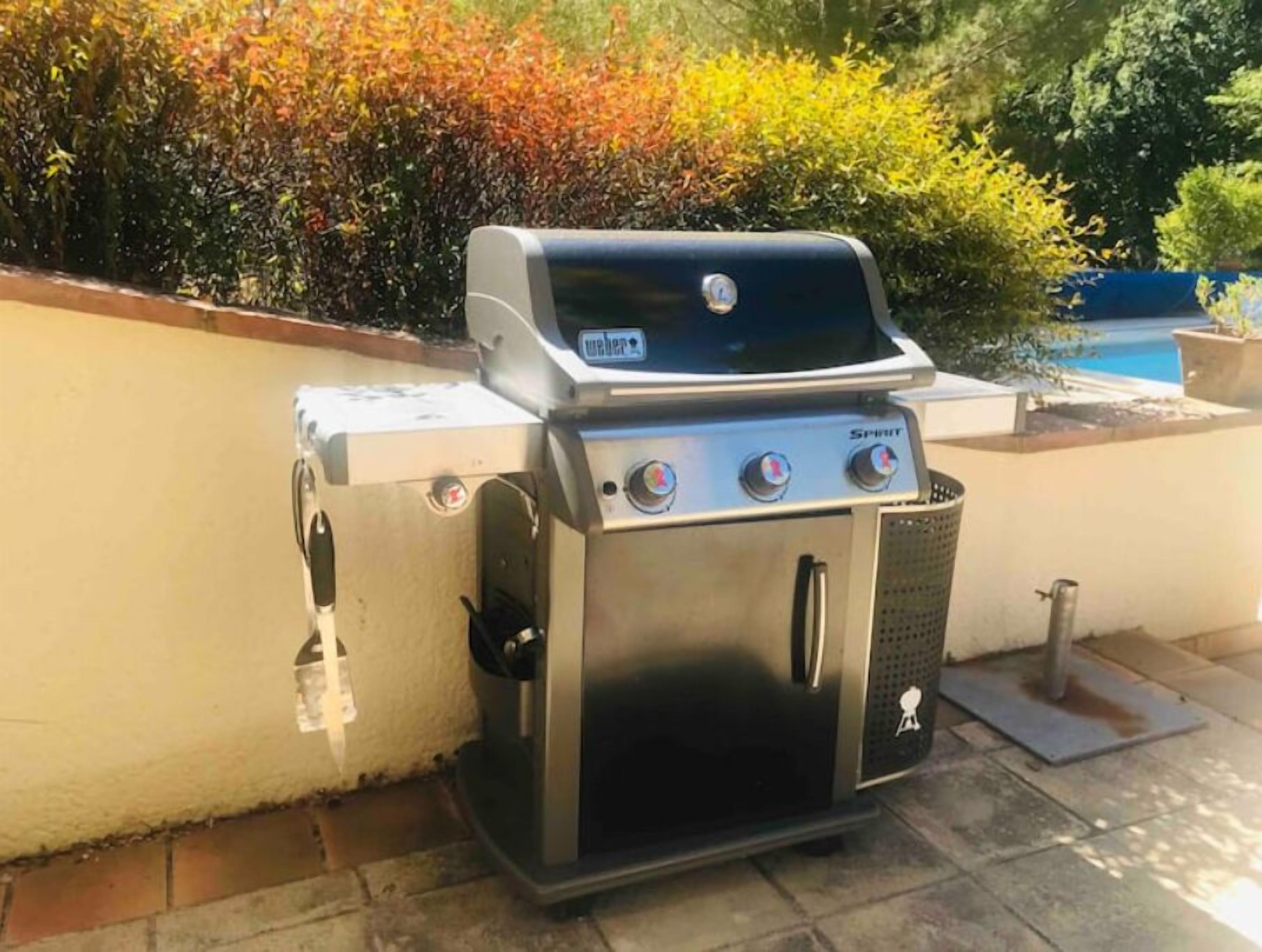 A stainless steel outdoor grill with a digital display, three control knobs, and a charcoal filter.