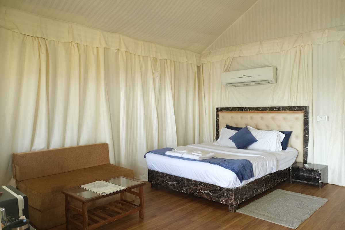 Quarto com cama, sofá, uma mesinha e aparelho de ar condicionado.