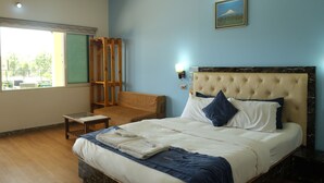 Ein Schlafzimmer mit einem Bett, einem Holzstuhl, einem kleinen Tisch und einem Fenster mit Blick auf Grünflächen.