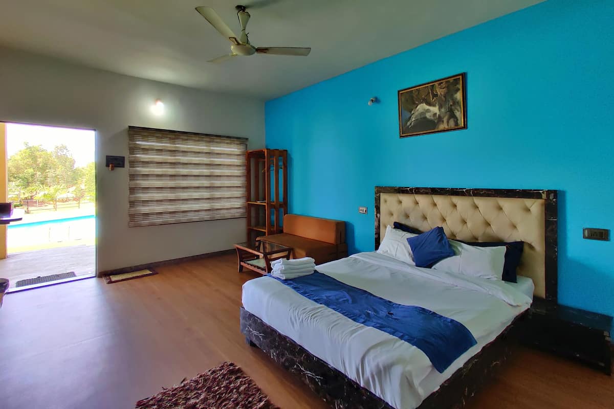 Quarto com cama, ventilador de teto, janela com persianas, prateleira de madeira e um quadro na parede.