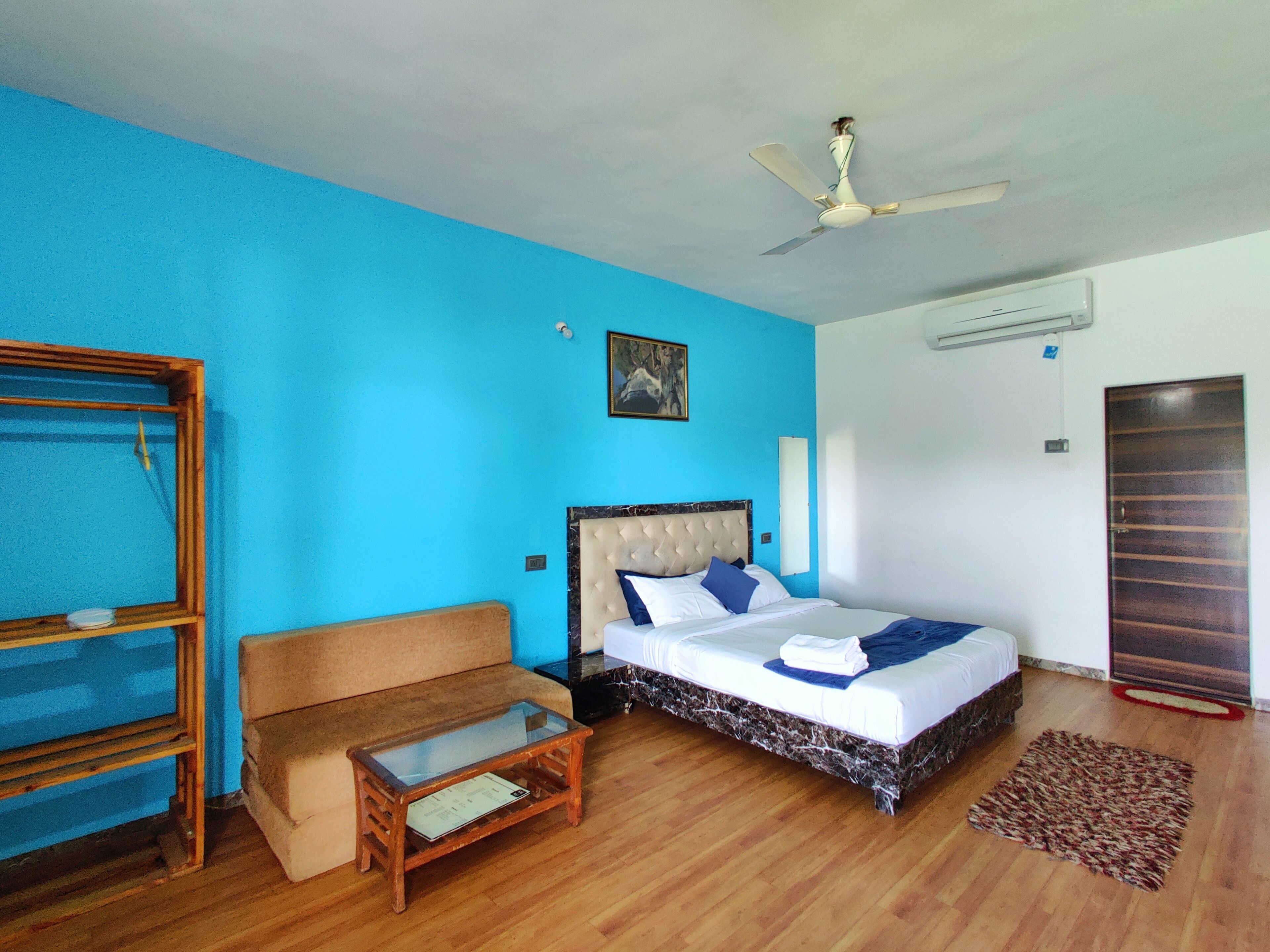 Une chambre  à coucher avec un lit, un banc en bois, un ventilateur de plafond et une porte.