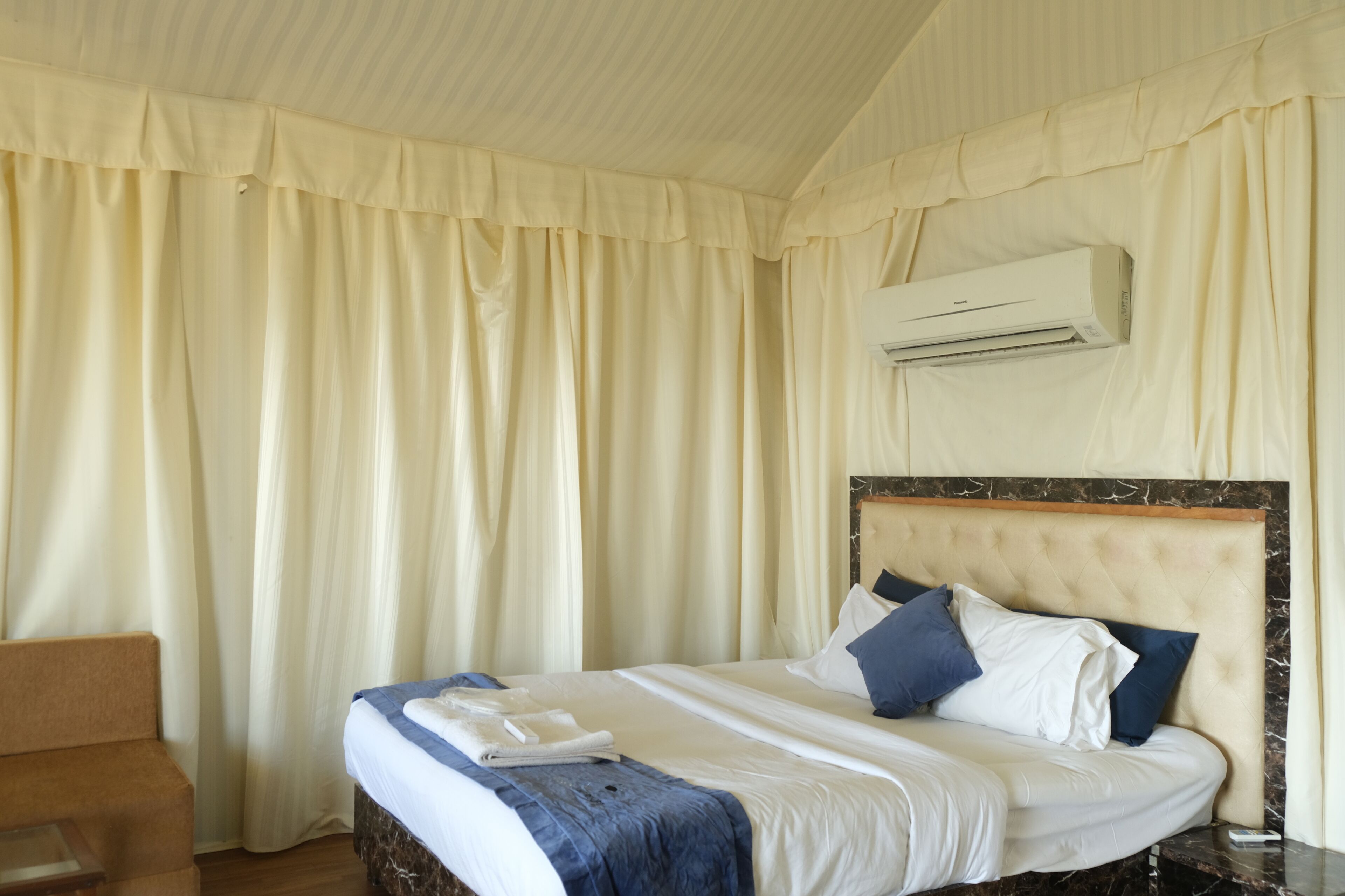 A hotel room with a bed, a chair, and an air conditioning unit.