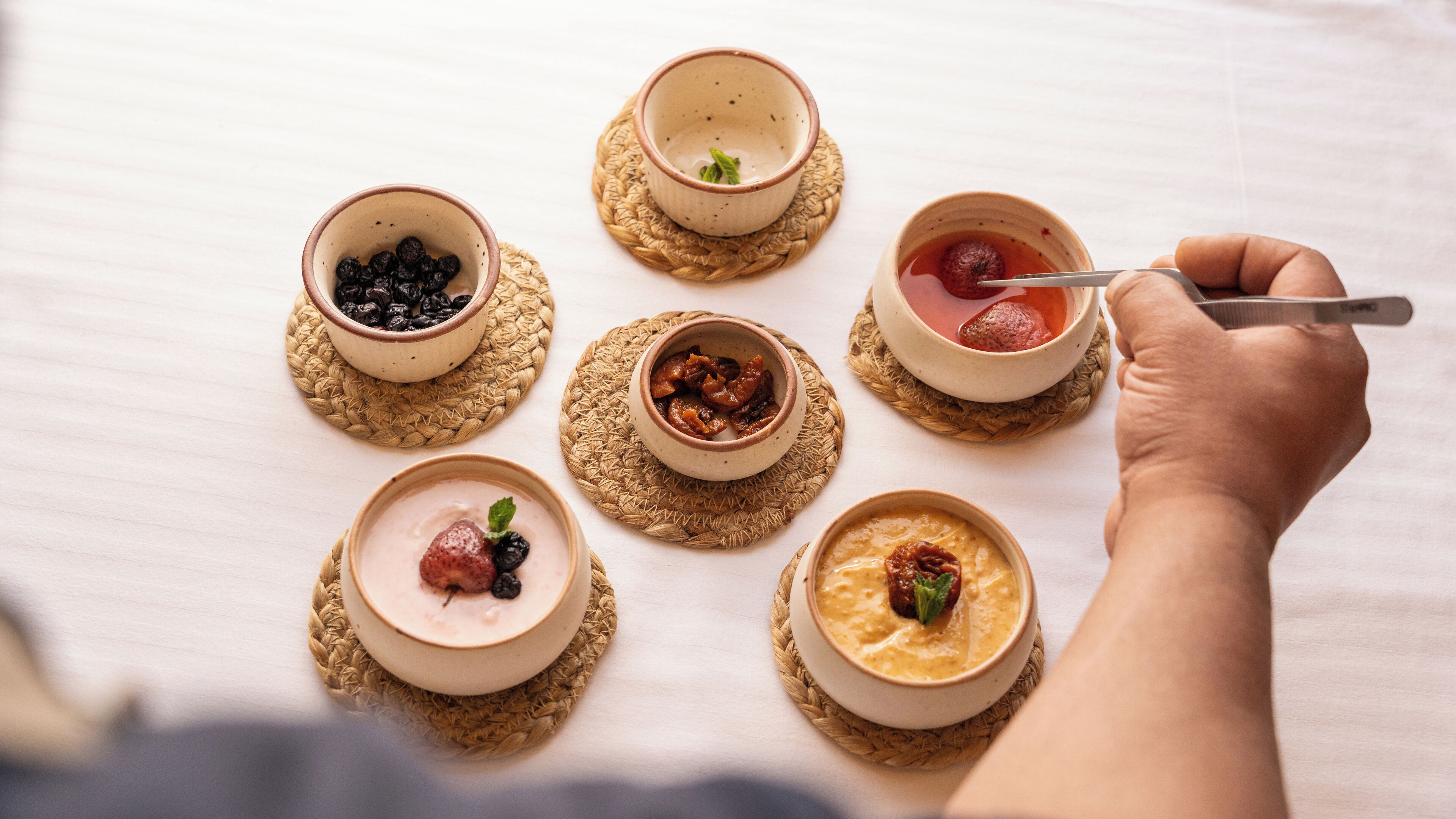 A table with six small bowls of food, each on a woven mat.