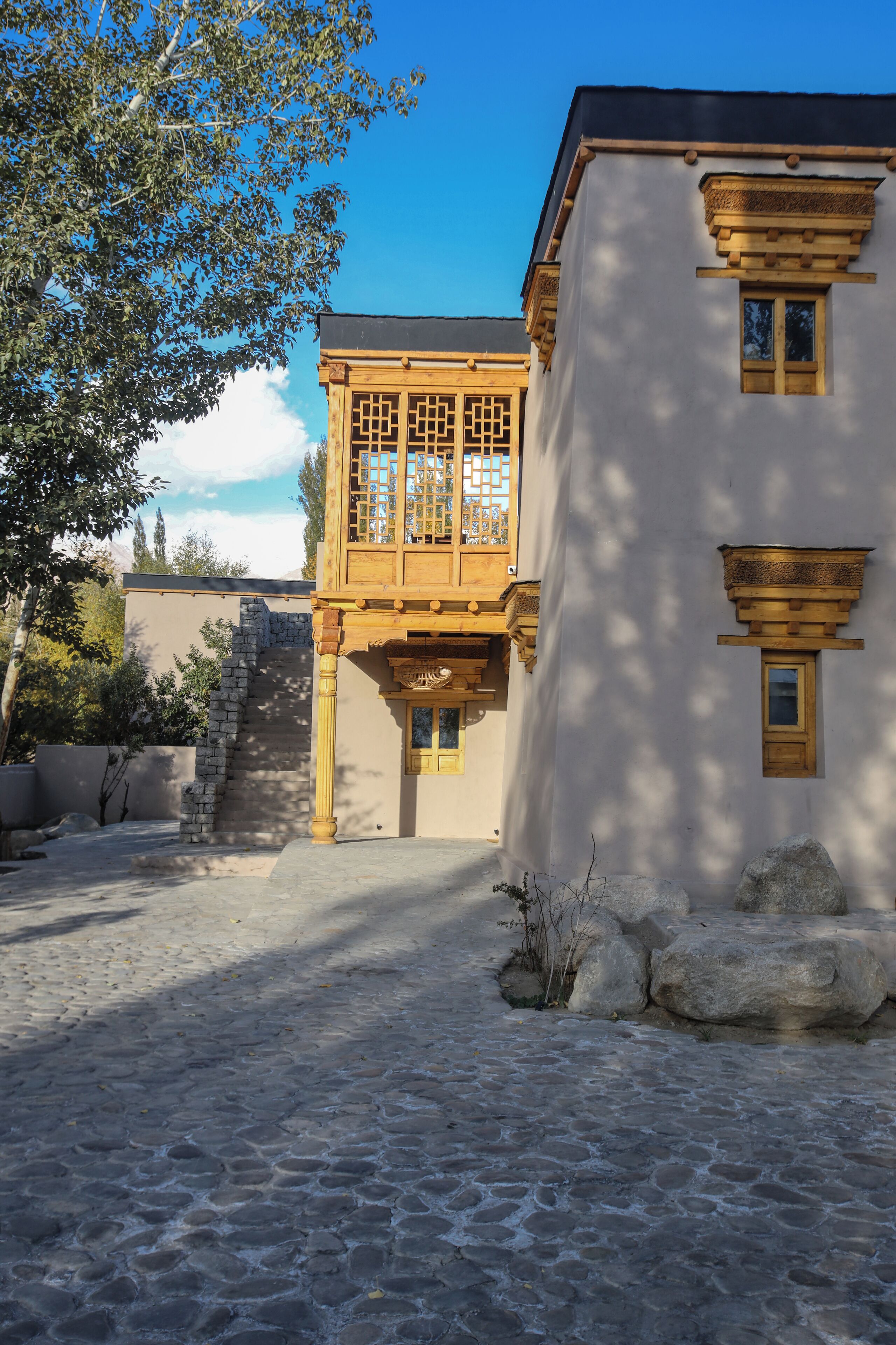A courtyard with a stone pathway leading to a building with traditional wooden balconies and a stone staircase.