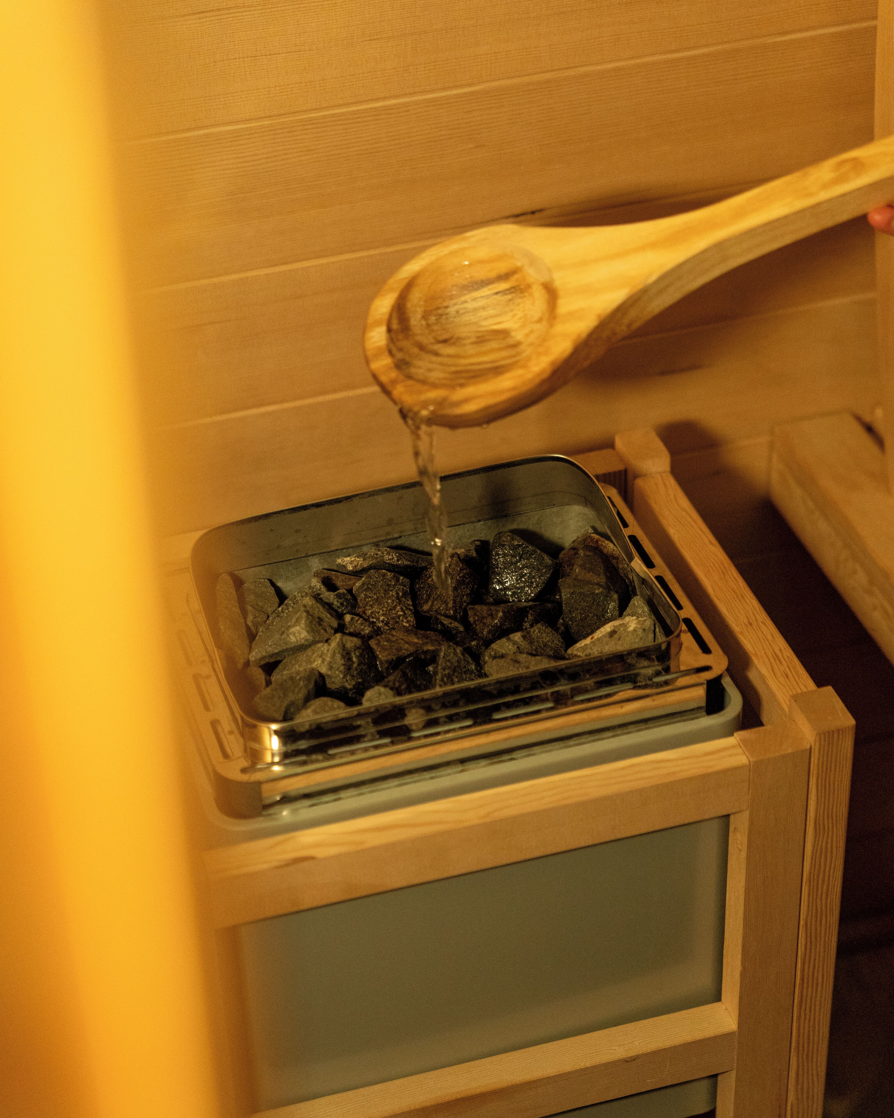 A wooden spoon pouring water over charcoal in a glass container.